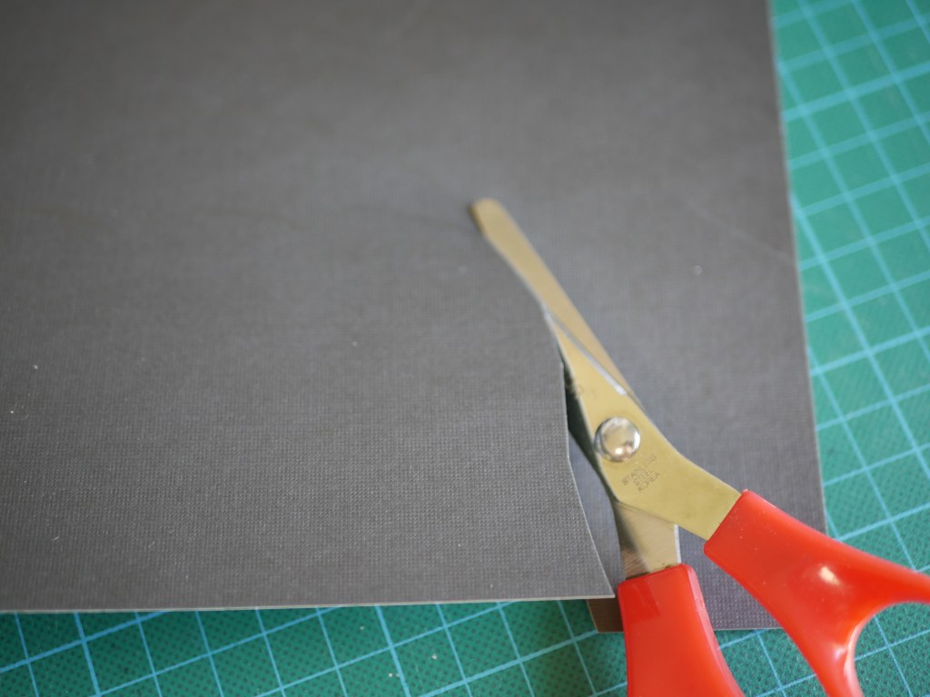 Scissors cutting black card into the shape of a bat wing.