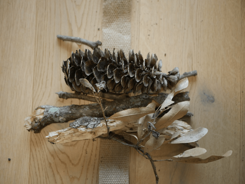 A collection of sticks, twigs, bark, leaves and a pine cone with a piece of jute twine underneath, ready to be tied together.